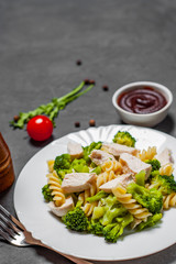 fusilli pasta with chicken breast and broccoli salad in white plate on Dark grey black slate background