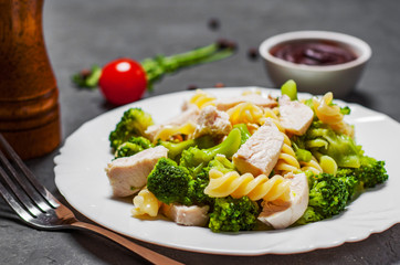 fusilli pasta with chicken breast and broccoli salad in white plate on Dark grey black slate background
