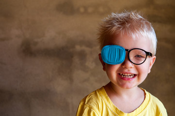 Portrait of funny child in new glasses with patch for correcting squint .Ortopad Boys Eye Patches nozzle for glasses for treatment of strabismus (lazy eye) - obrazy, fototapety, plakaty