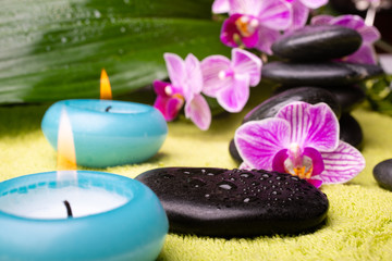 spa concept. a lit candle in the foreground, and stones with orchids in the background