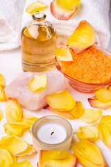 Wellness center. Composition with orange-flavored bath salts, transparent glass bottle with perfumed essential oil, white towels, rose petals and candle.