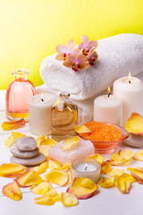 At the center of the table are the transparent bottles with oil and perfumed essences, orange-flavored bath salts, white towels, rose petals, orchids, some stones and candles.