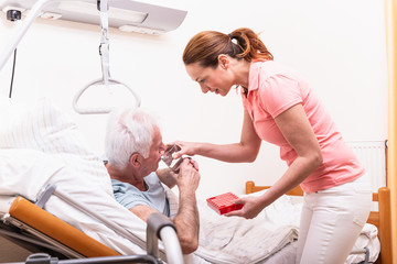 Junge Pflegerin im Altenheim Pflegepersonal reicht altem Mann ein Glas Wasser und Medikamente