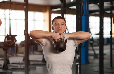 Fototapeta na wymiar Fit And Concentrated Young Man Training With Kettlebell in Gym.