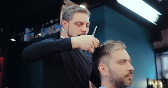 Male barber making client haircut with scissors. Brutal men's hair salon.