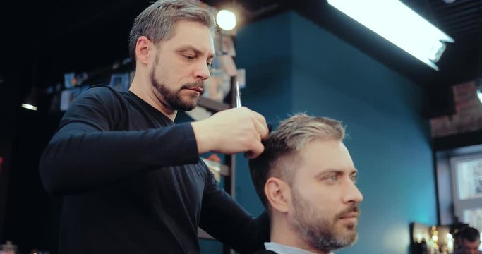 Brutal barber scissors man's hair in a salon. Stylish hairdresser.