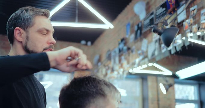 Male stylist working in a hair salon. Makes a haircut to the client.