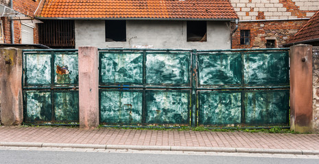 Bardzo stara metalowa brama pomalowana n azieolno.  Zadrzewila i odrapana.