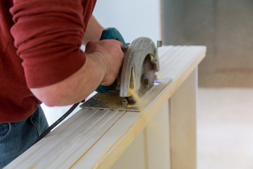 Man hands holding circular saw and preparing to make a cut wood door