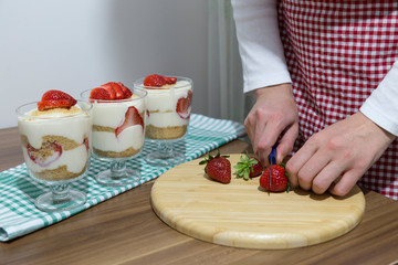 layered dessert or Magnolia with strawberries, biscuit cake and cream cheese on a white wood background.