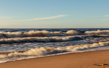 Golden yellow foamy sea waves background at romantic beach sunset with endless horizon
