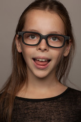 Fototapeta na wymiar Portrait of an eight-year-old girl with a calm mood, in a black blouse and glasses with black rim. Studio photo session