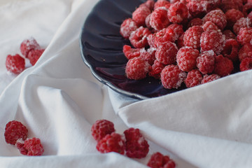 Fresh raspberries on a dark blue beautiful plate on a white background and on a napkin. The concept of vegetarianism and healthy eating
