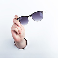 Female hand out of the hole in the paperman, holding sunglasses for vision. Isolate on white background.
