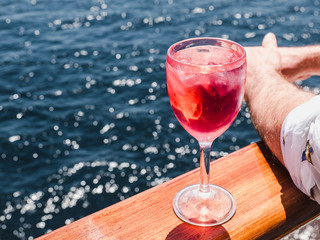 Beautiful wineglass with a pink cocktail and ice cubes, standing on the open deck against the...