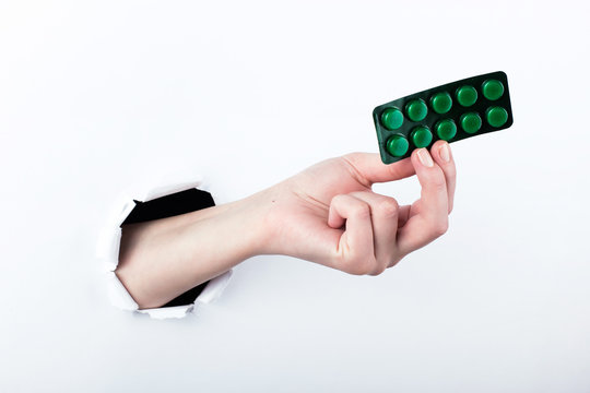 Female hand out of the hole in the paperman, holding blisters with pills. Isolate on white background.