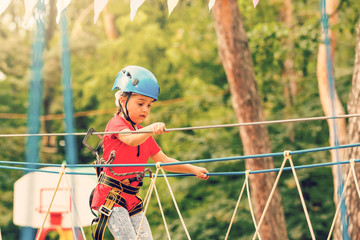 Portrait of cute little girl walk on a rope bridge in an adventure rope park.