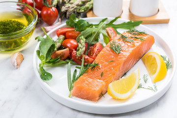 Fresh salmon pieces with salad,herbs and lemon on plate