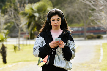 Attractive young woman enjoying her time outside in park. play mobile phone, listen music