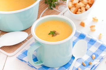 Pumpkin soup in blue enamelled mug with pumpkin seeds, horizontal