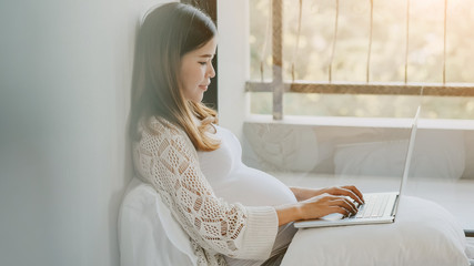 Pregnant  woman sitting at the bed and working on the laptop computer.