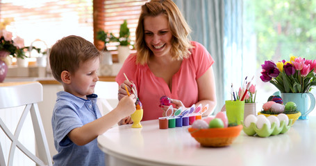 Happy young mother and son are painting Easter eggs