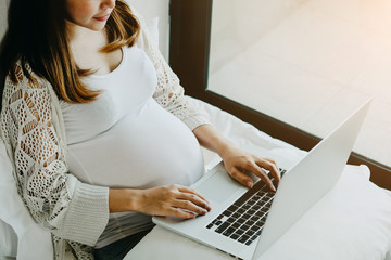 Naklejka premium Pregnant woman sitting at the bed and working on the laptop computer.