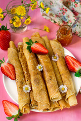 Stack of thin pancakes served with strawberries and daisy flowers