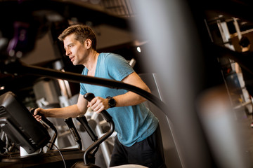 Man doing exercise on elliptical cross trainer in sport fitness gym club