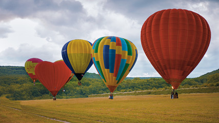 Fototapeta premium Five Hot Air Ballons Taking off in front of green hills and field