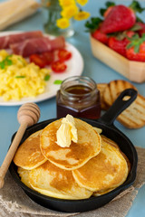 Pancakes with butter served with scrambled eggs and ham for breakfast