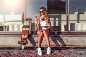 Girl sits summer city background building, her hand telephone online application Internet,...
