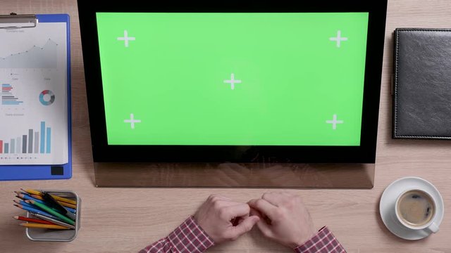 Top view of man's hands scrolling over the left edge of a green screen touch monitor. Office and corporate concept. Big chroma key.