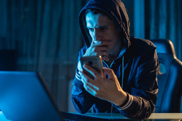 Male hacker in the hood holding the phone in his hands trying to steal access databases with...