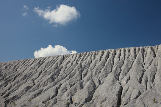 Slope of an abandoned slagheap covered ravines against the blue sky. Mining industry.