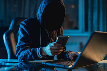 Anonymous hacker programmer uses a laptop to hack the system in the dark. Concept of cybercrime and...