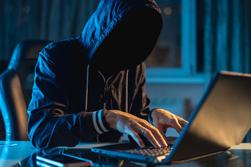 Anonymous hacker programmer uses a laptop to hack the system in the dark. Concept of cybercrime and...