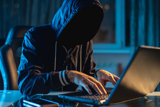 Anonymous hacker programmer uses a laptop to hack the system in the dark. Concept of cybercrime and hacking database