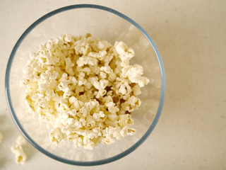 Popcorn on a table in focus, popcorn in a glass bowl out of focus. Top view.