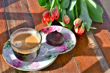 a saucer with a cup of coffee and a cake and a bouquet of tulips lie on a wooden table
