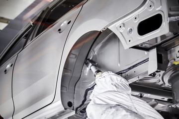 The robots in the car manufacturing plant are helping the car body to be glued at the seams.