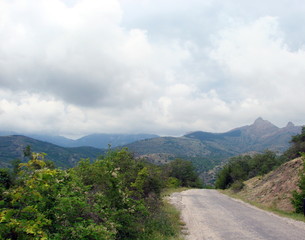 Landscape of flowering mountain forests on both sides of the road on the background of the blue ridges of the Crimean mountains on a horizon under the cloudy summer sky.