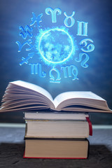 Open book on astrology on a dark background. The glowing magical globe with signs of the zodiac in...