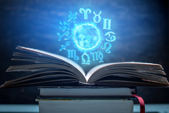 Open book on astrology on a dark background. The glowing magical globe with signs of the zodiac in the blue light