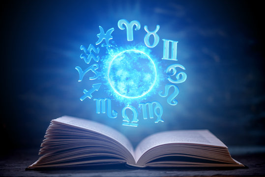 Open book on astrology on a dark background. Glowing magical globe with signs of the zodiac in the blue light.