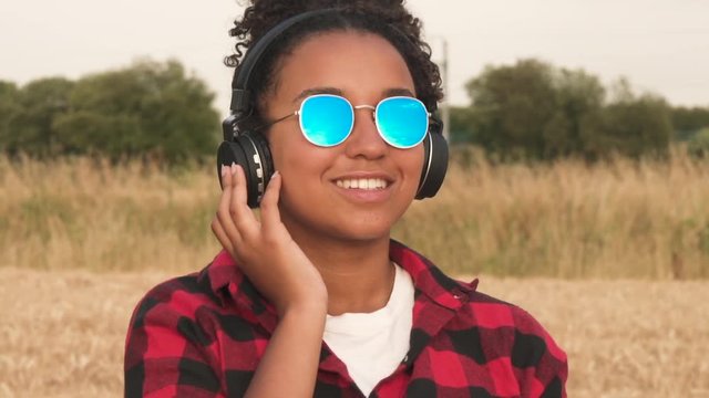 Slow motion HD video clip of beautiful mixed race African American girl teenager young woman outdoors wearing blue sunglasses listening to music on wireless headphones