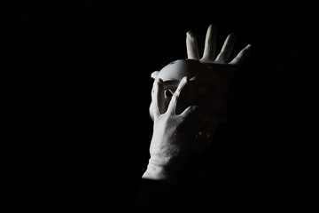 White scary mask on a black background with whites hand.
