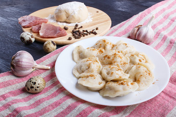 Dumplings with ingredients (meat, dough, spices) on a linen tablecloth on a black wooden background.