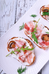 Bruschetta with pancetta, cream cheese, roasted champignons and arugula on a white plate
