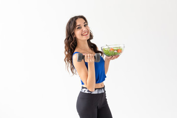 Healthy lifestyle, people and sport concept - Healthy young woman with vegetables and dumbbells...